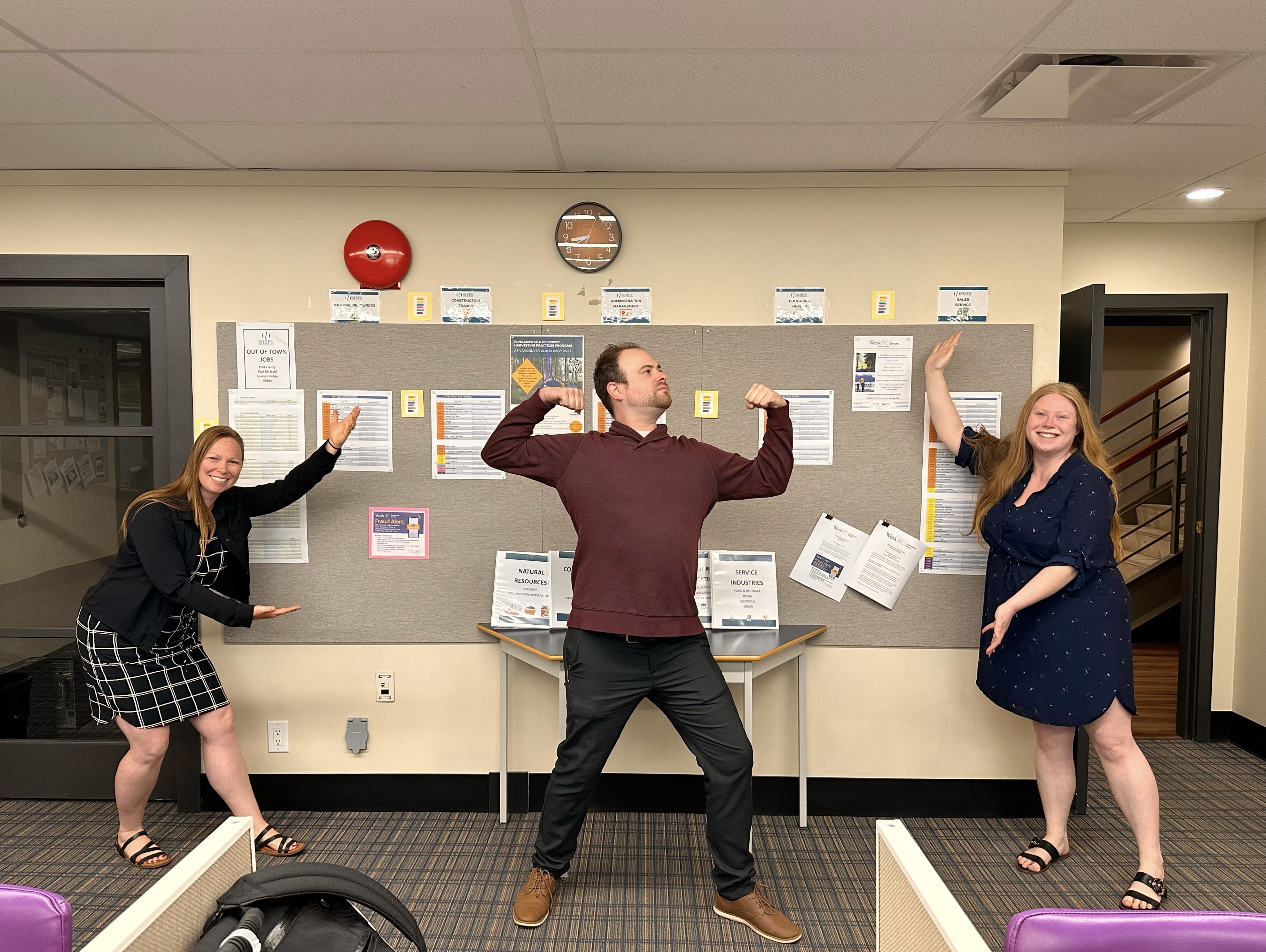 # staff members in silly poses showing off their work on the in-house job board in our Campbell River location