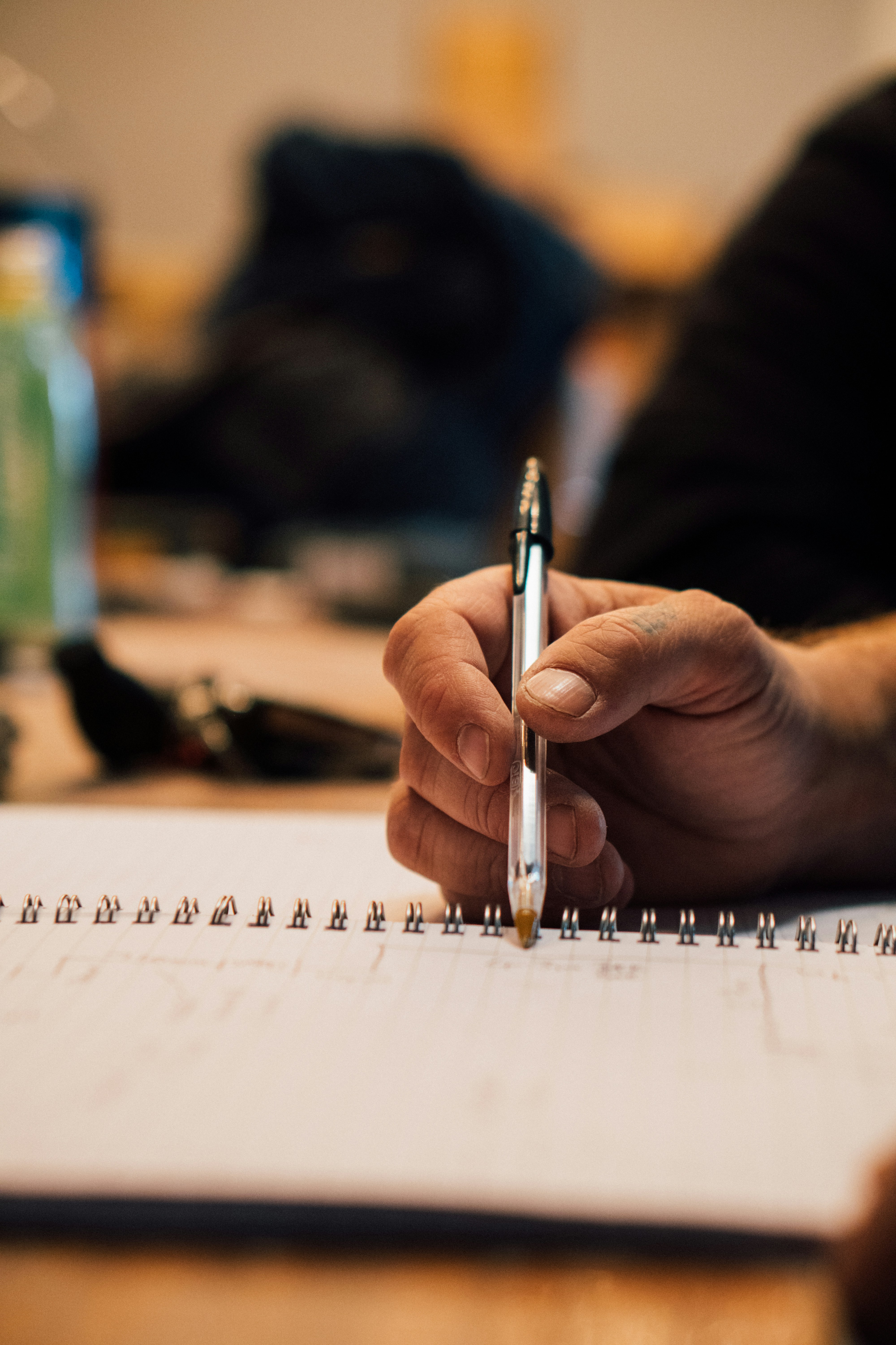 hand of a person holding a pen and making notes in a spiral coil note book.