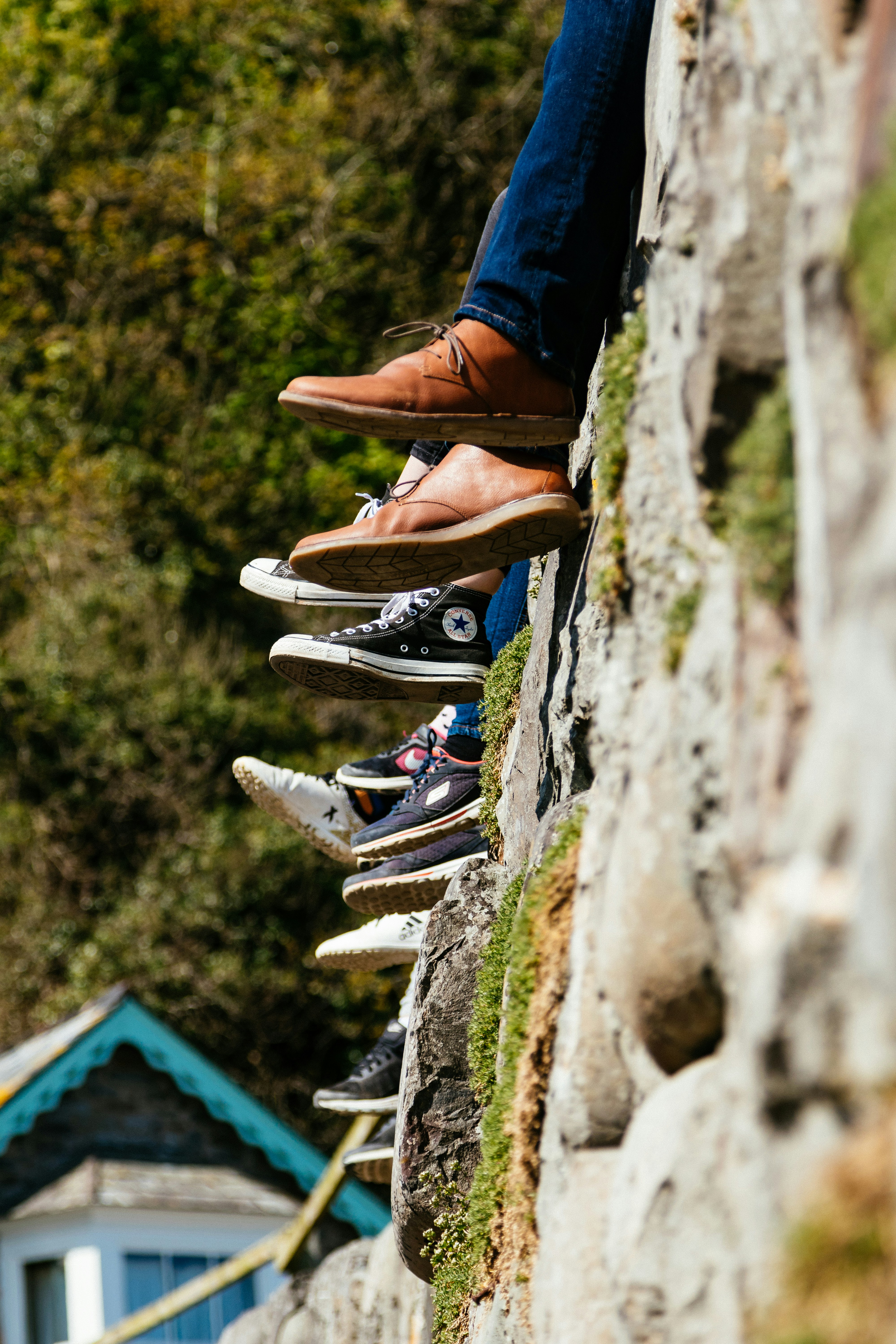 group p of people sitting on a stone wall , you can only see their shoes