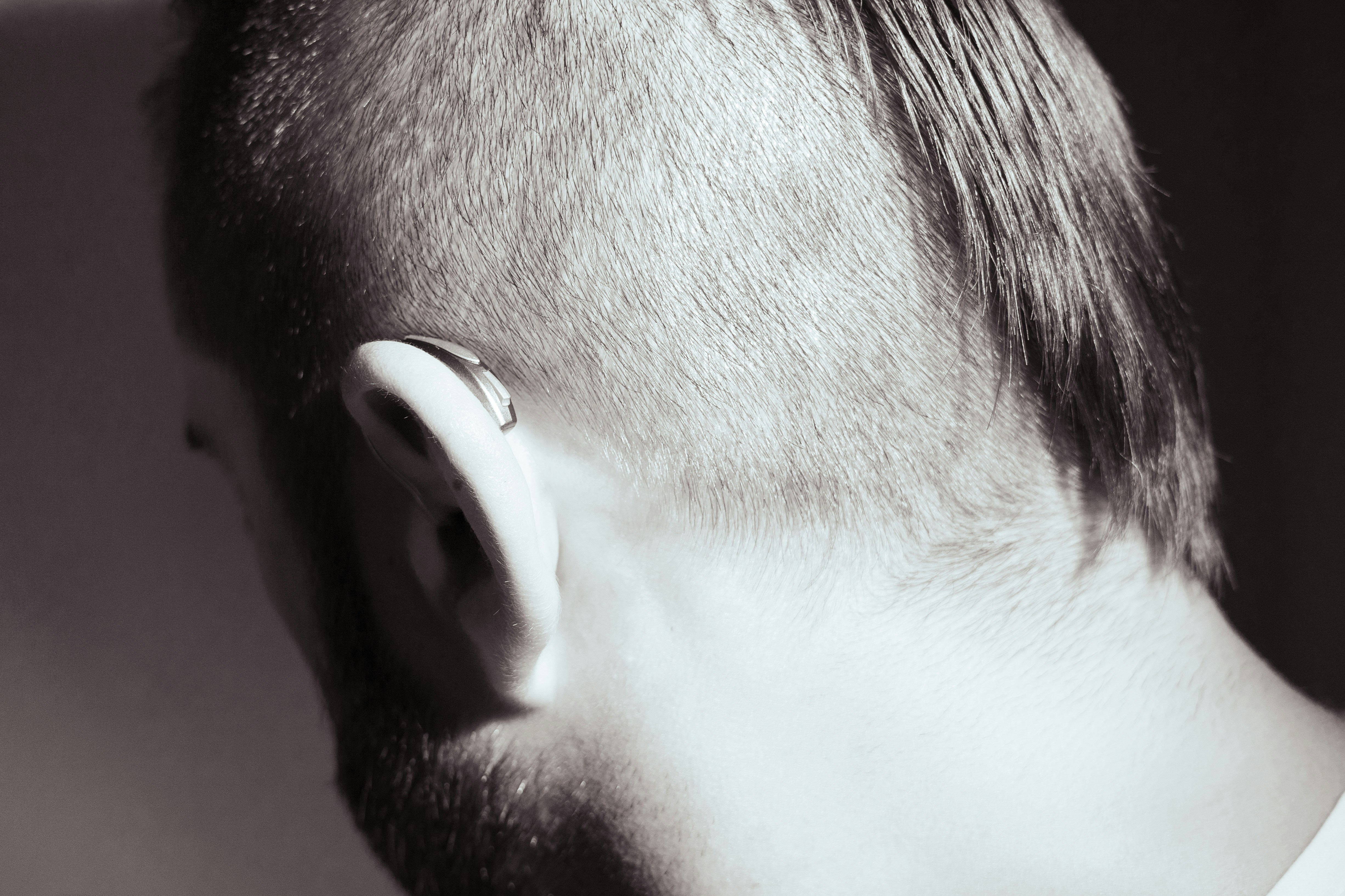man with shaved hair style that exposes a small hearing aid behind his left ear
