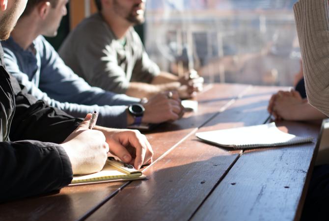 people sitting at a wooden table with pens and a note pad