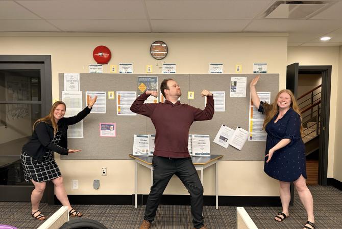 # staff members in silly poses showing off their work on the in-house job board in our Campbell River location