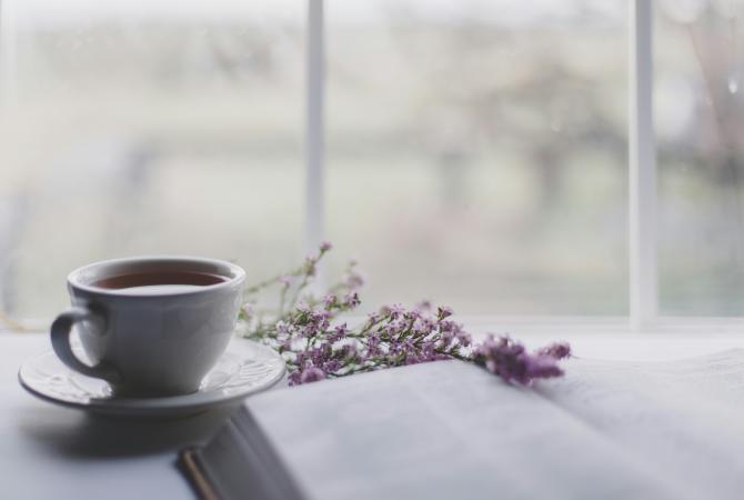 a cup of tea on a table beside a sprig of lavender and a book