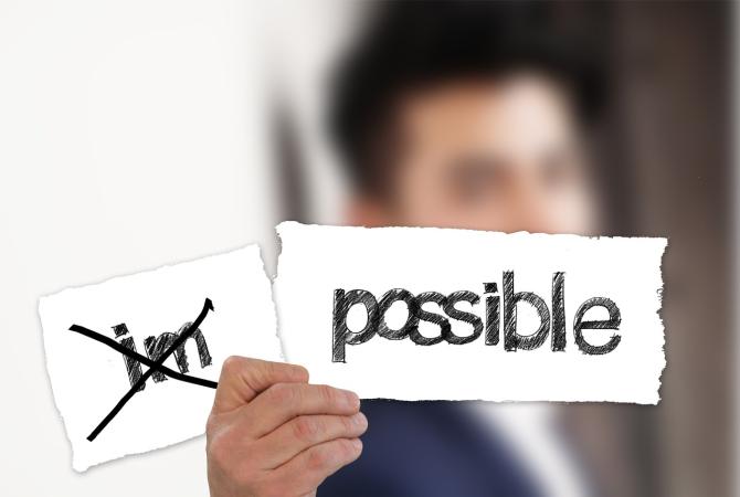 person holding a sign that has been torn into 2 parts, one that reads IM, the other Possible